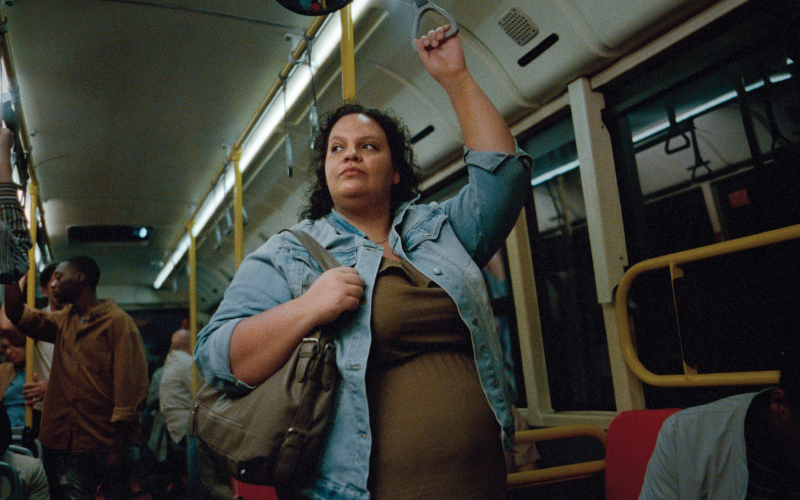 Women standing on a bus or subway wearing a jean jacket and green dress.