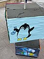 Happy Tux painting holding a grey fish on a cardboard box used as a decoration for a college event.
