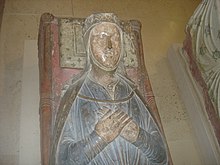 A photograph of a medieval tomb with a carving of Isabella on top. She is lying with her hands clasped, wearing a blue dress.