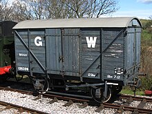 A short goods van built from planks of wood. The sides are mid-grey with a large white G to the left of the doors and a large white W to the right.