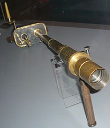 A brass telescope attached to rectangular goggles connected to a candle-holder and some intricate sights to look through.
