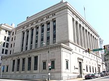 A seven-story sandstone building faced with ionic columns on a city street corner.