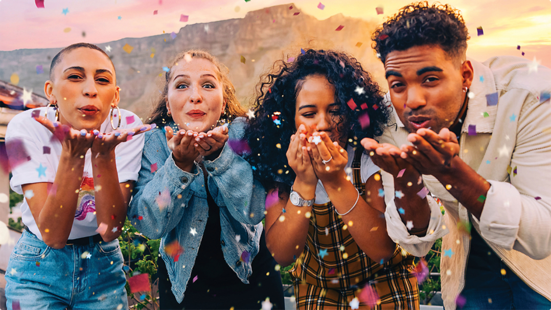 Four people outdoors blowing confetti out of their hands