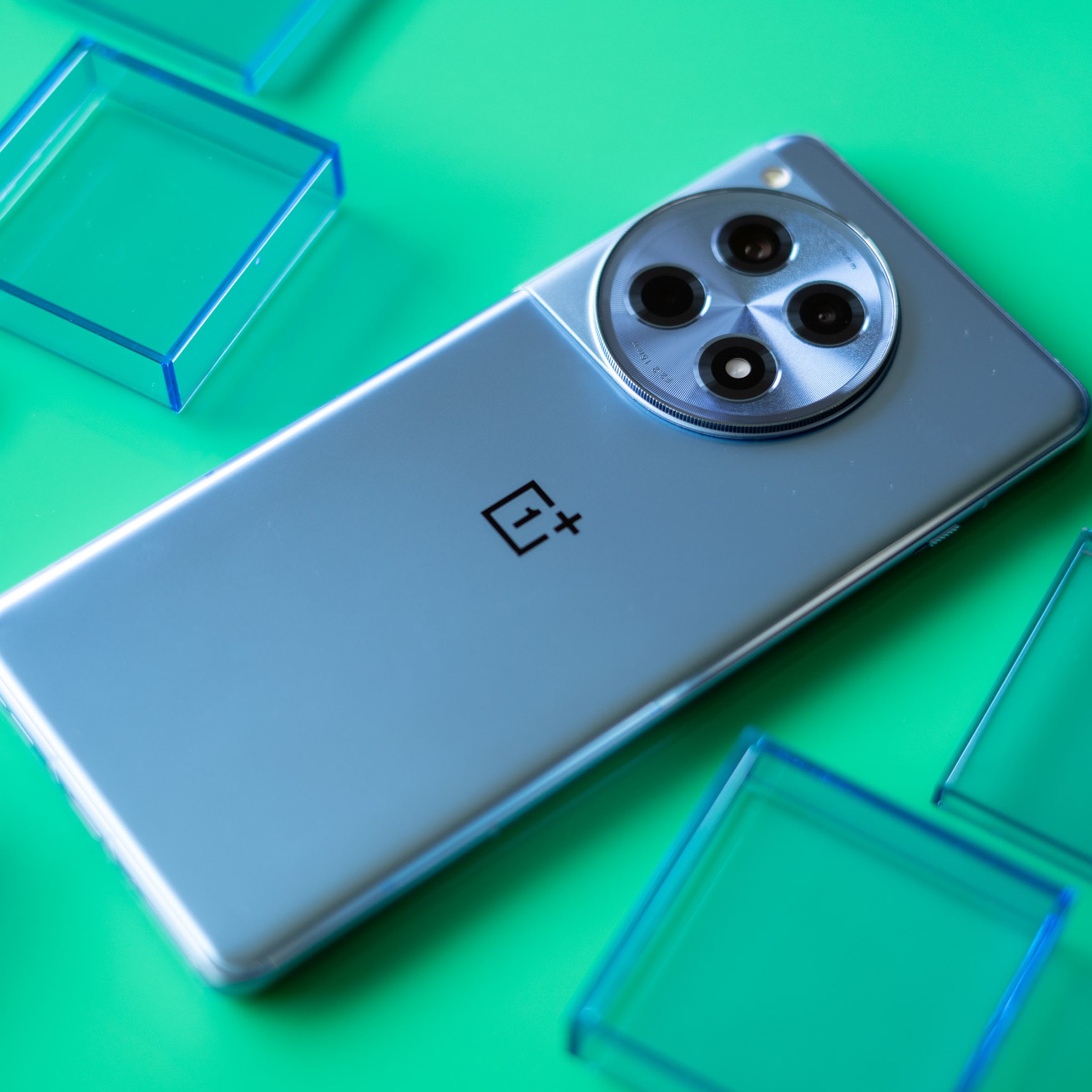 OnePlus 12R on a green background with back panel facing up surrounded by blue translucent squares.