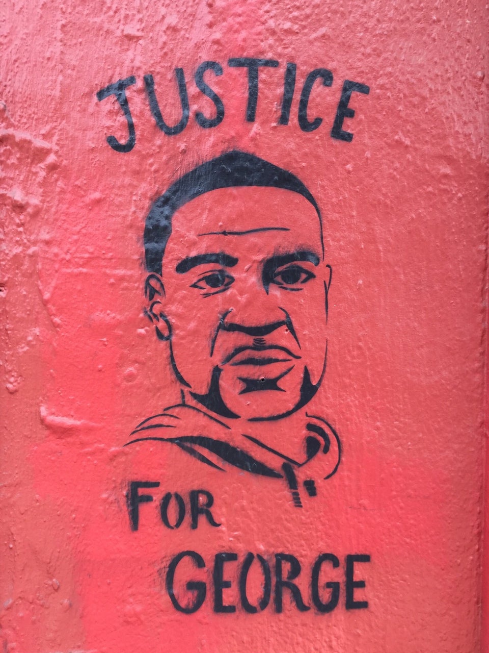 Stencil street art of George Floyd on a red wall with the word JUSTICE above his head, and FOR GEORGE below.