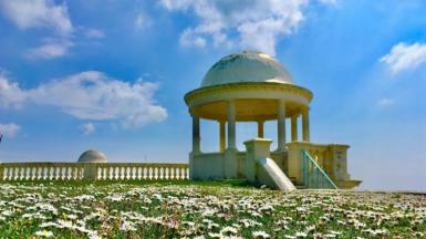 A bandstand with blue skies and a few fluffy clouds overhead, with daisies in the foregroundq