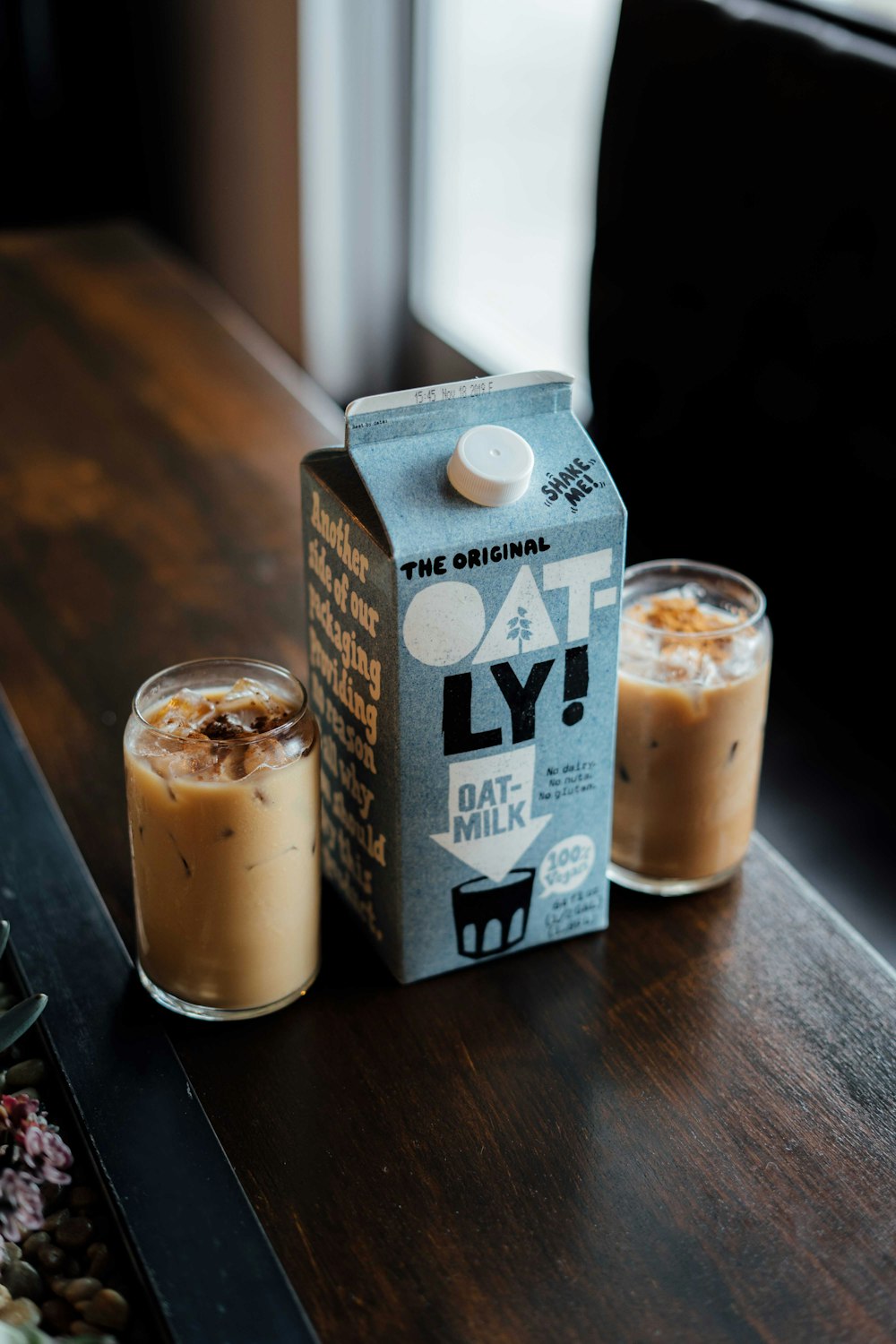 a carton of oatly next to two glasses of oatmeal