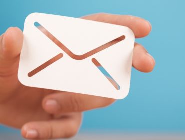 A hand holding a white email icon envelope against a blue background.
