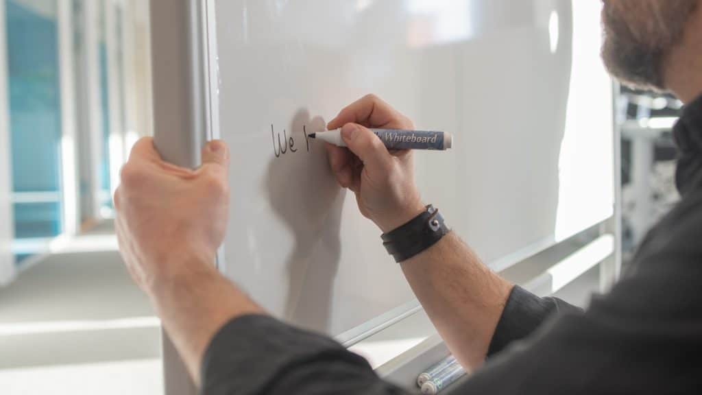 Närbild av en man som skriver på en whiteboardtavla.