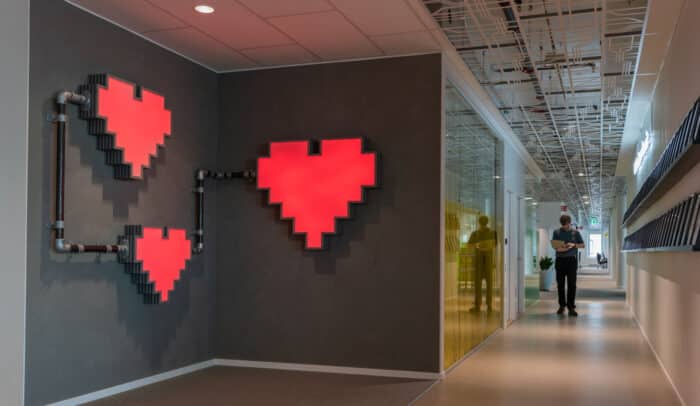 Internetstiftelsens hjärtan i röd neon på en vägg, i korridoren vid sidan syns en man med laptop.