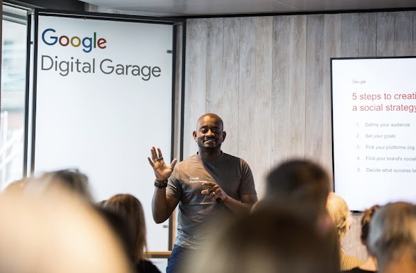 Man stood in front of a 'Google Digital Garage' sign, speaking to a group of people.