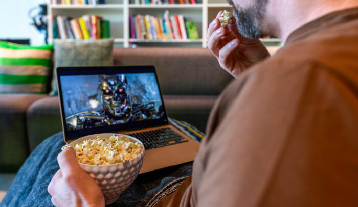 Man sitter vid en laptop och tittar på en ai-genererad bild, han äter popcorn.