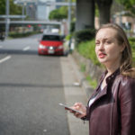 A young white female wating on the roadside in central Tokyo, for a taxi or ride.