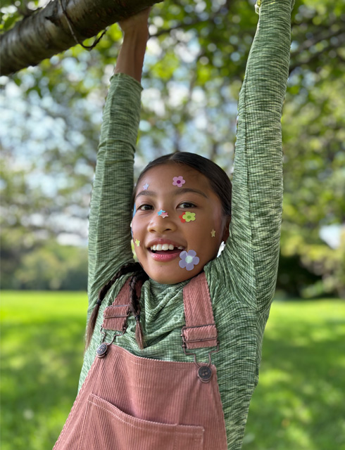Närbild på en flicka med blommiga klistermärken i ansiktet, tagen med 2× tele med optisk kvalitet på iPhone 15