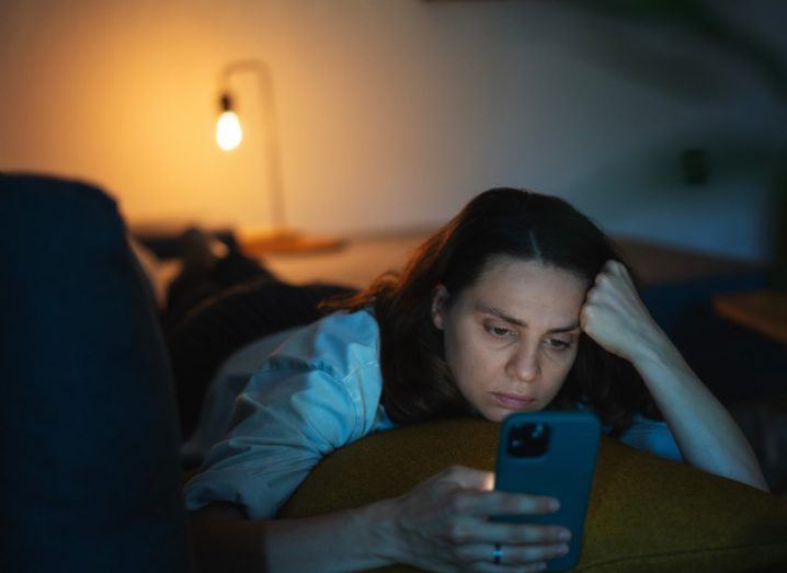 A woman lies in bed scrolling on her phone at night.